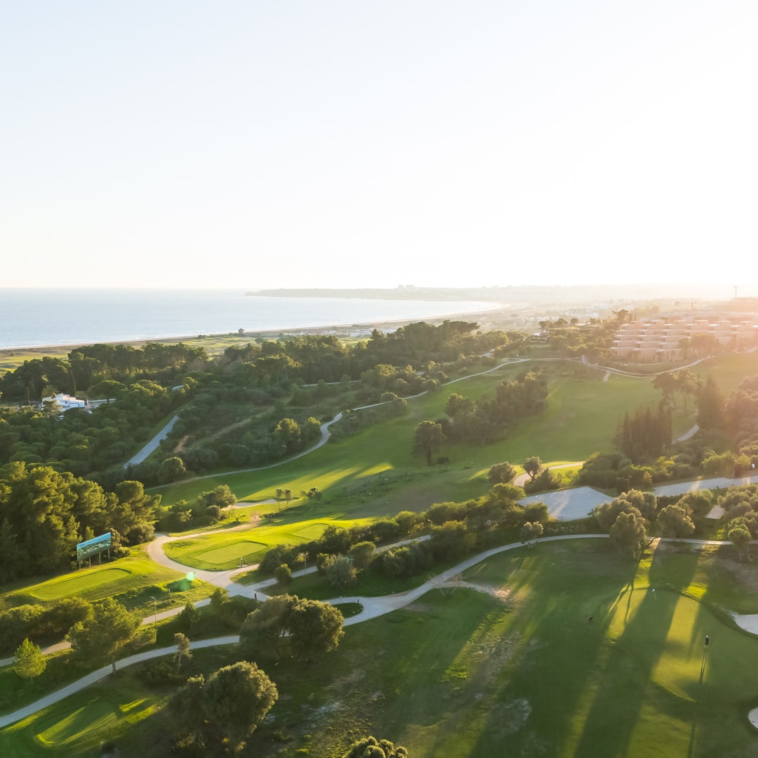 Sunlit aerial view of Palmares Golf near Lagos, featuring coastal fairways and clubhouse in Algarve, Portugal.