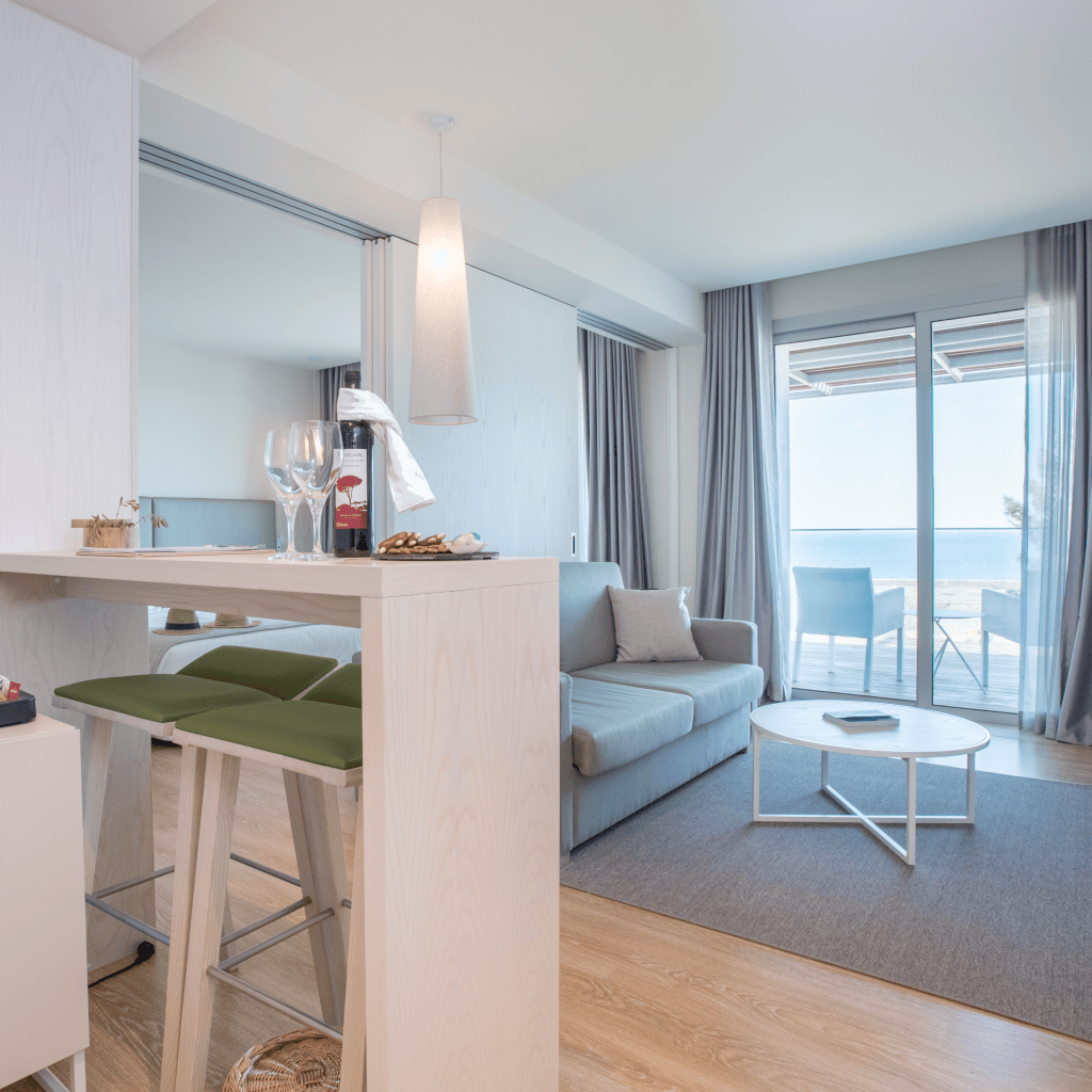 Sala de estar luminosa com acesso à varanda e vista para o mar, no Palmares Beach House Hotel.