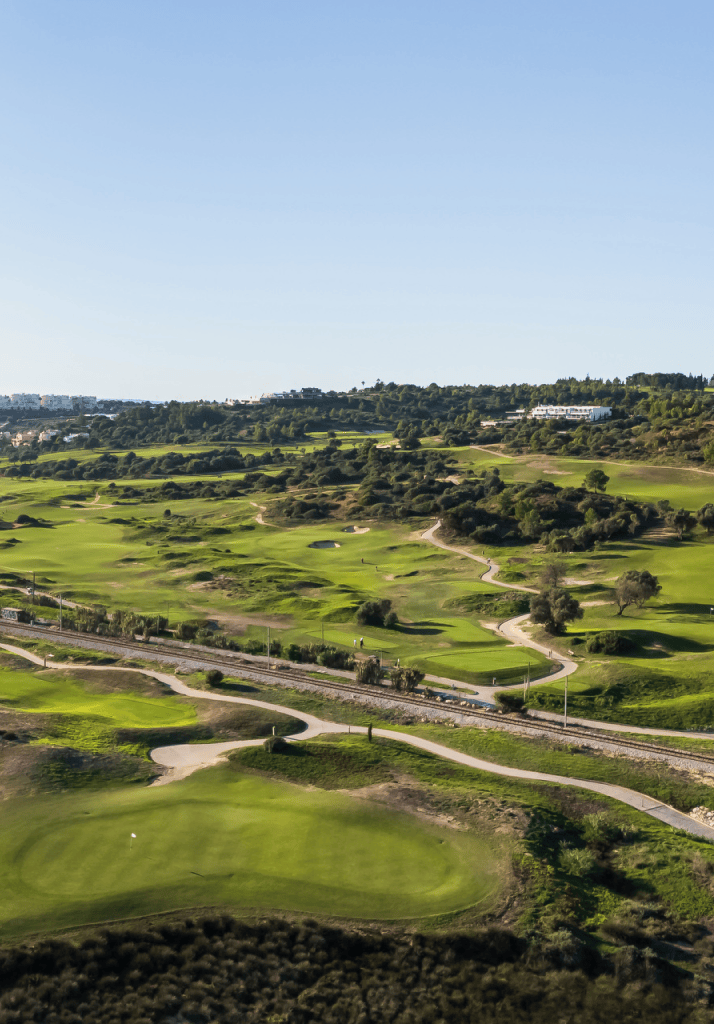Vista aérea dos fairways do campo de golfe do Palmares, com Lagos ao fundo e vegetação natural envolvente.
