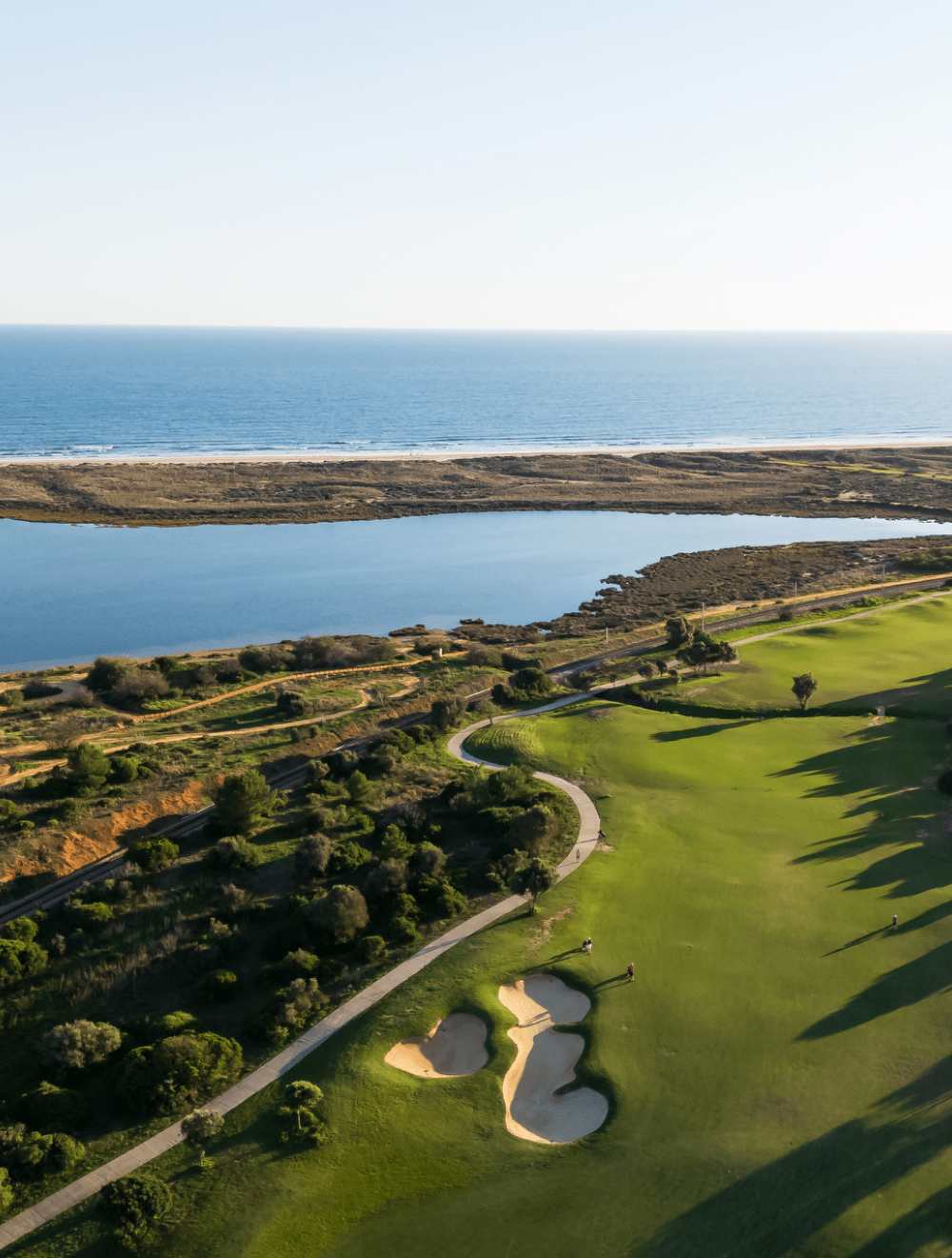 Vista aérea do campo de golfe de Palmares junto à costa do Algarve, com o mar e a ria de Lagos ao fundo, numa paisagem onde o desporto se funde com a natureza.