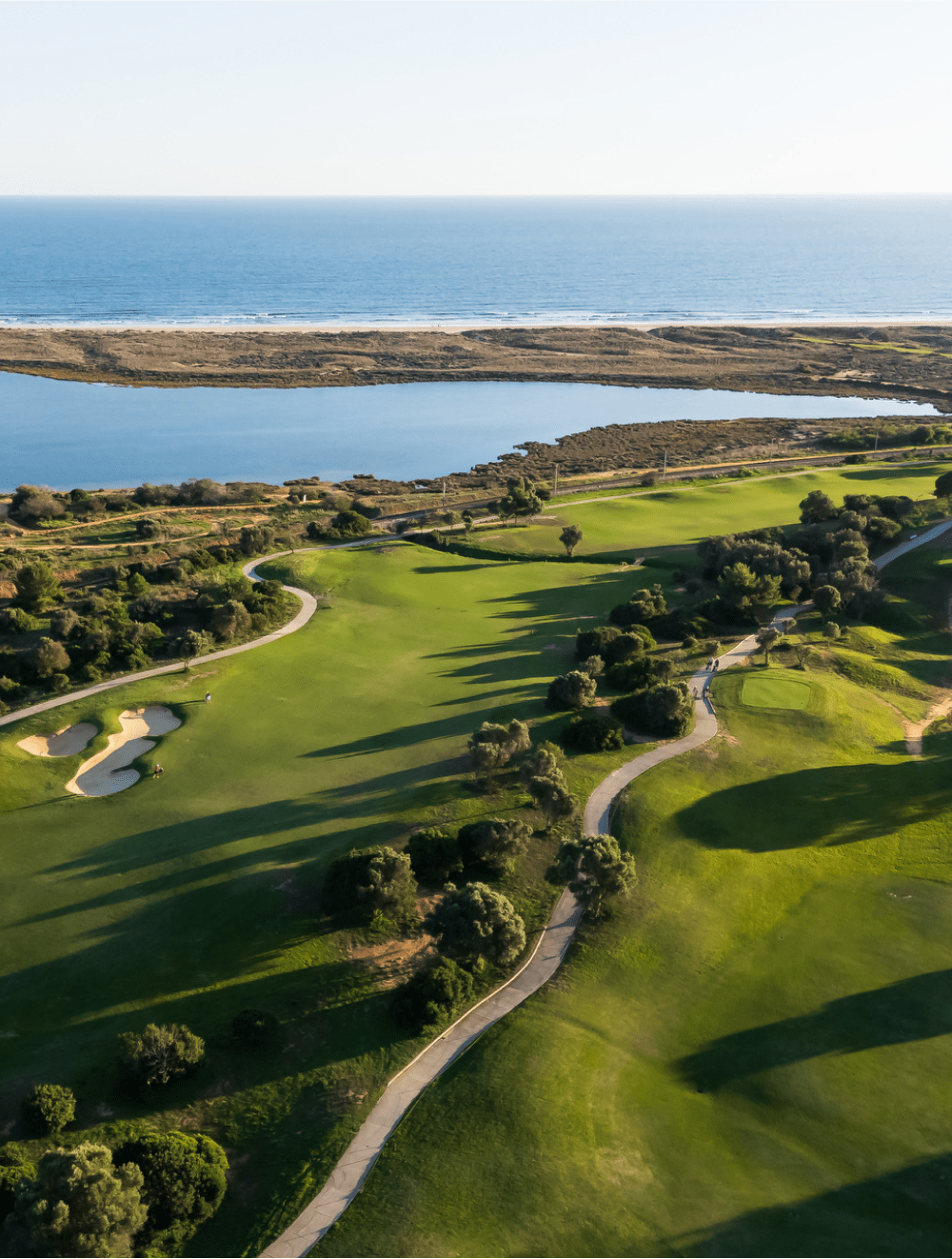Campo de golfe de Palmares iluminado pela luz dourada da tarde, com vista para a ria de Lagos e o Oceano Atlântico — elegância natural num resort de excelência no Algarve.