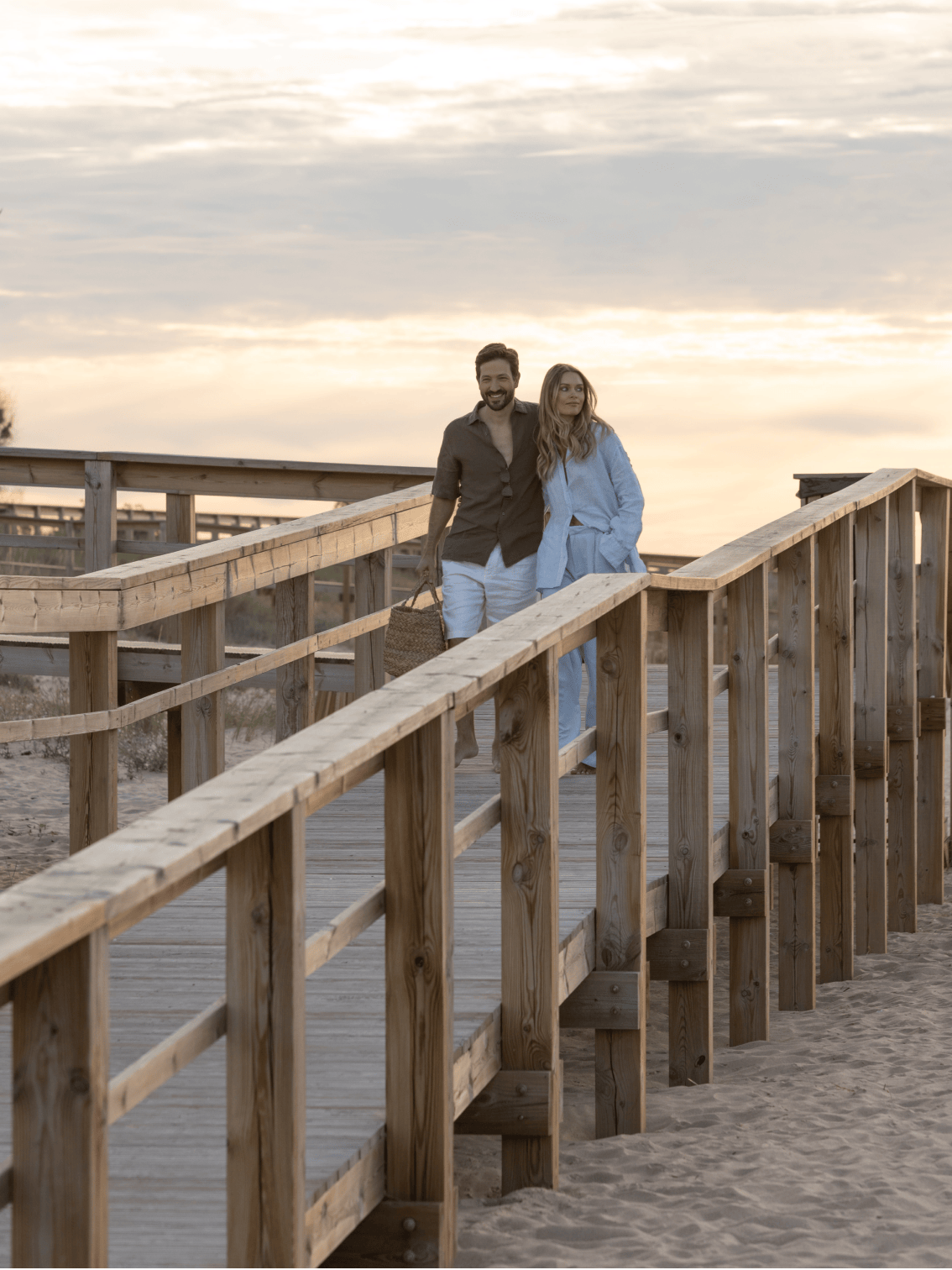 Casal a passear ao pôr do sol na passadeira de madeira com acesso à praia de Palmares.