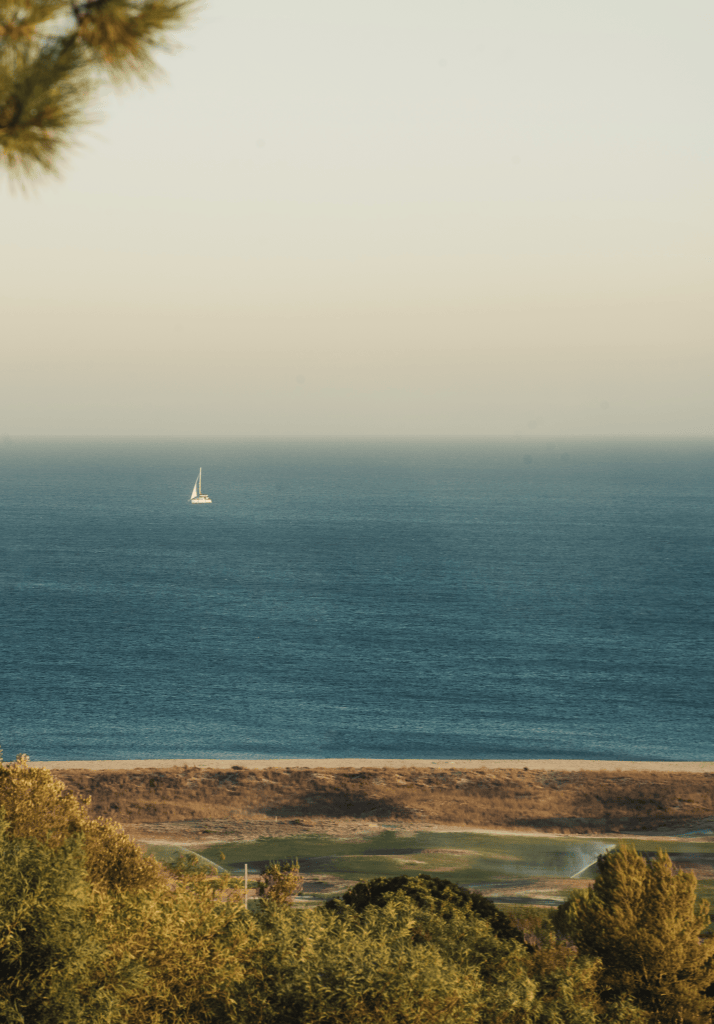Veleiro ao longe na costa de Alvor, visto do Palmares Resort com campo de golfe e natureza em primeiro plano.