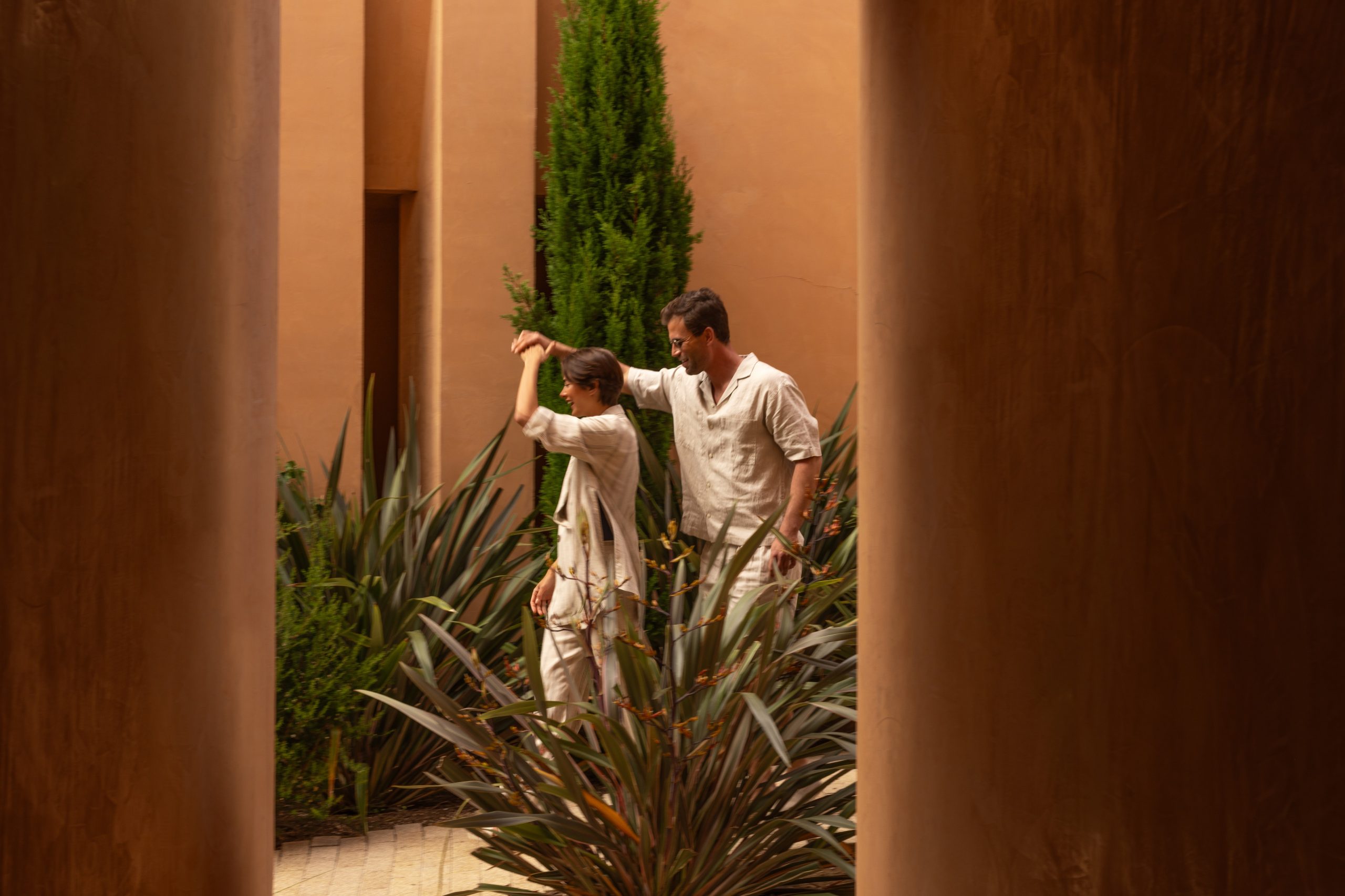 Couple enjoying a peaceful walk through the lush gardens of Palmares Ocean Living & Golf, Algarve, surrounded by elegant Mediterranean architecture.